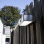 Moderne, eckige Lutec LED Solar-Wandleuchte Brick aus Edelstahl an Holzzaun.