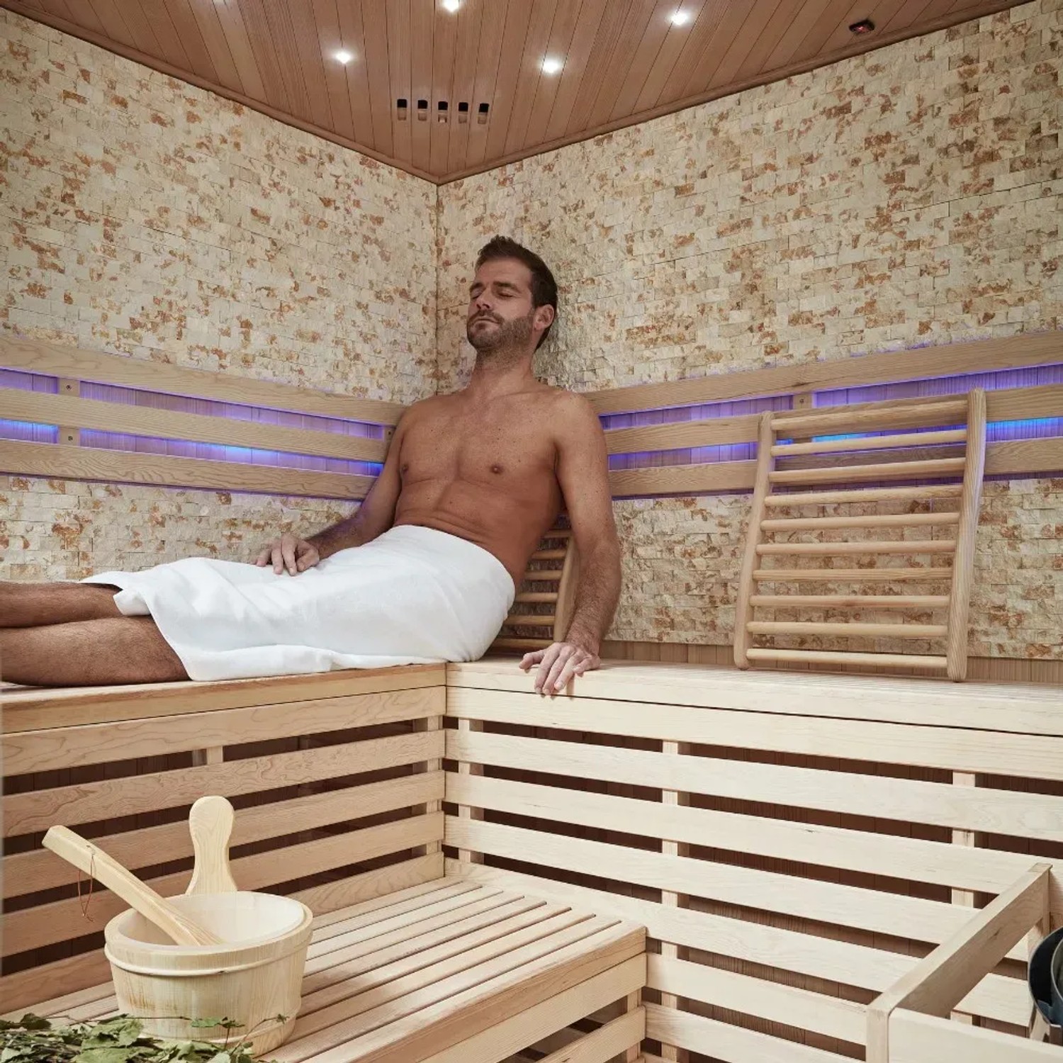 Entspannung in der SKYLINE BIG Sauna: Tannenholz, Kunststeinwand, mit Saunazubehör und liegender Person.