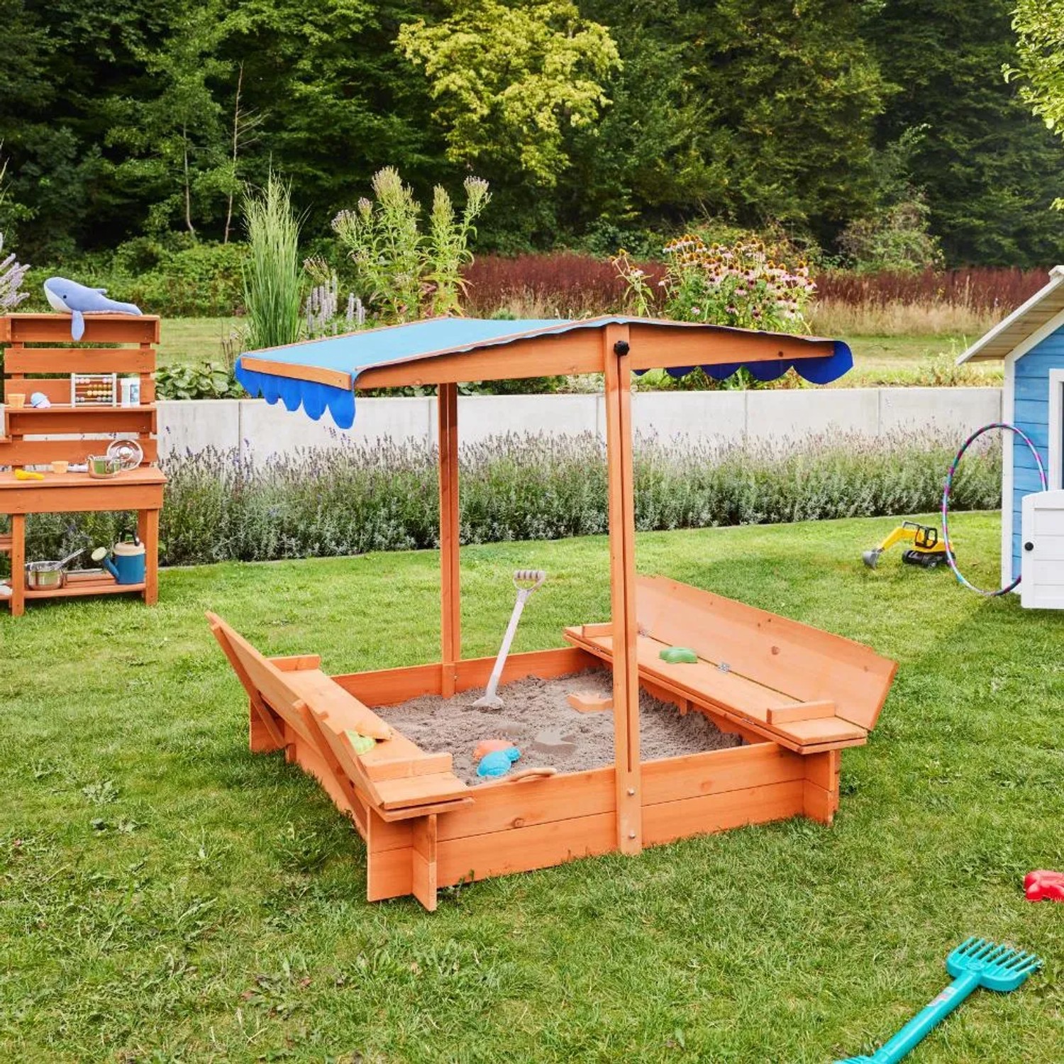 Holz Sandkasten Buddelkiste mit blauem Dach und Sitzbänken im Garten.