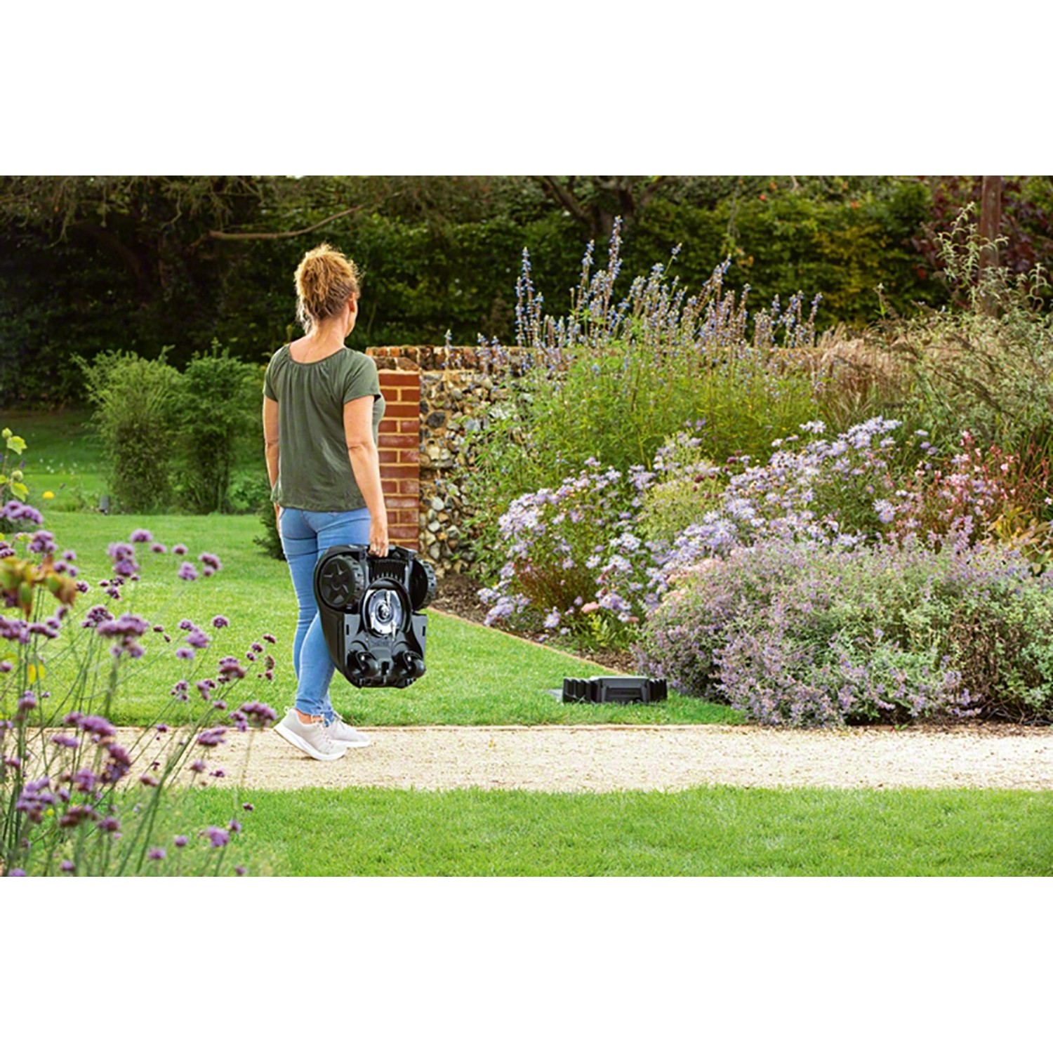 Frau trägt Bosch Mähroboter Indego XS 300 durch den Garten.