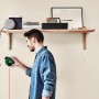 Mann benutzt Bosch Atino Linienlaser mit Maßband zum Ausrichten an einer Wand.