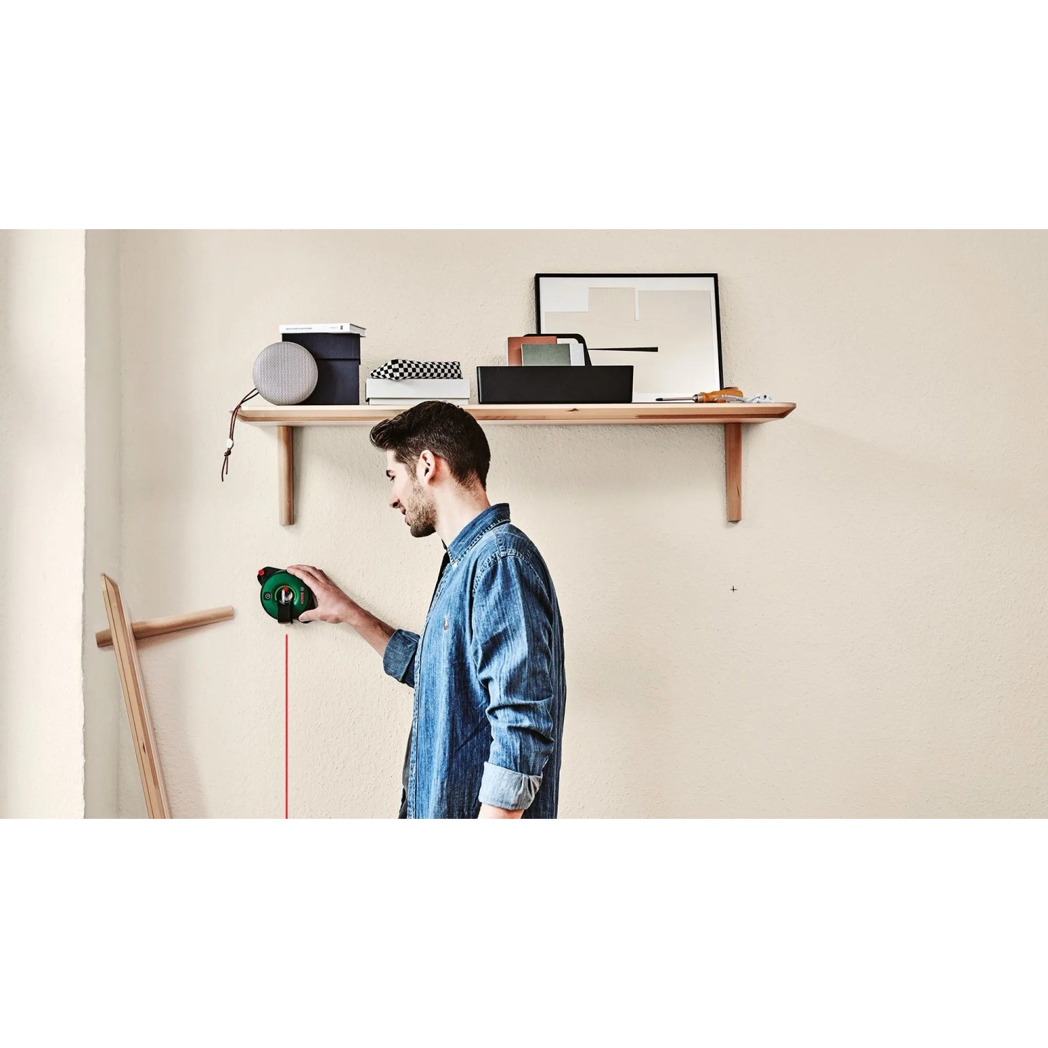 Mann benutzt Bosch Atino Linienlaser mit Maßband zum Ausrichten an einer Wand.
