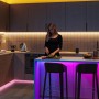 Moderne Küche mit Philips Smart-LED-Beleuchtung. Frau kocht bei warmweißem und farbigem Licht. GU10 Leuchtmittel für individuelle Lichtstimmung.