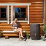 Garantia Regentonne Barrica 260 l in Dunkelbraun vor Holzhaus mit Frau auf Bank.