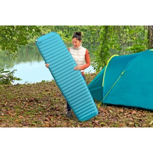 Frau hält blaue Single-Isomatte TerrainPro™ (183x51x5,1 cm) neben Zelt. Camping & Outdoor Zubehör.