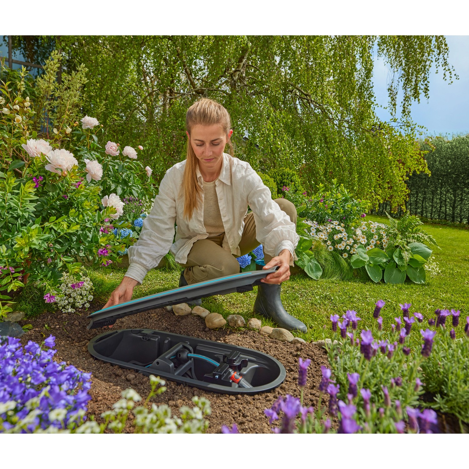 Frau öffnet Gardena Undercover Schlauchbox RollUp M im Garten, Komplettset zur unterirdischen Schlauchaufbewahrung.