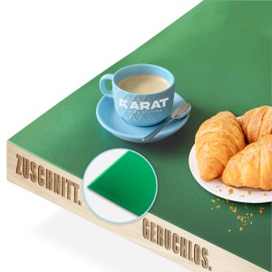 Grüne KARAT Tischfolie Empire mit abgeschrägter Kante, mit Kaffee und Croissants dekoriert.