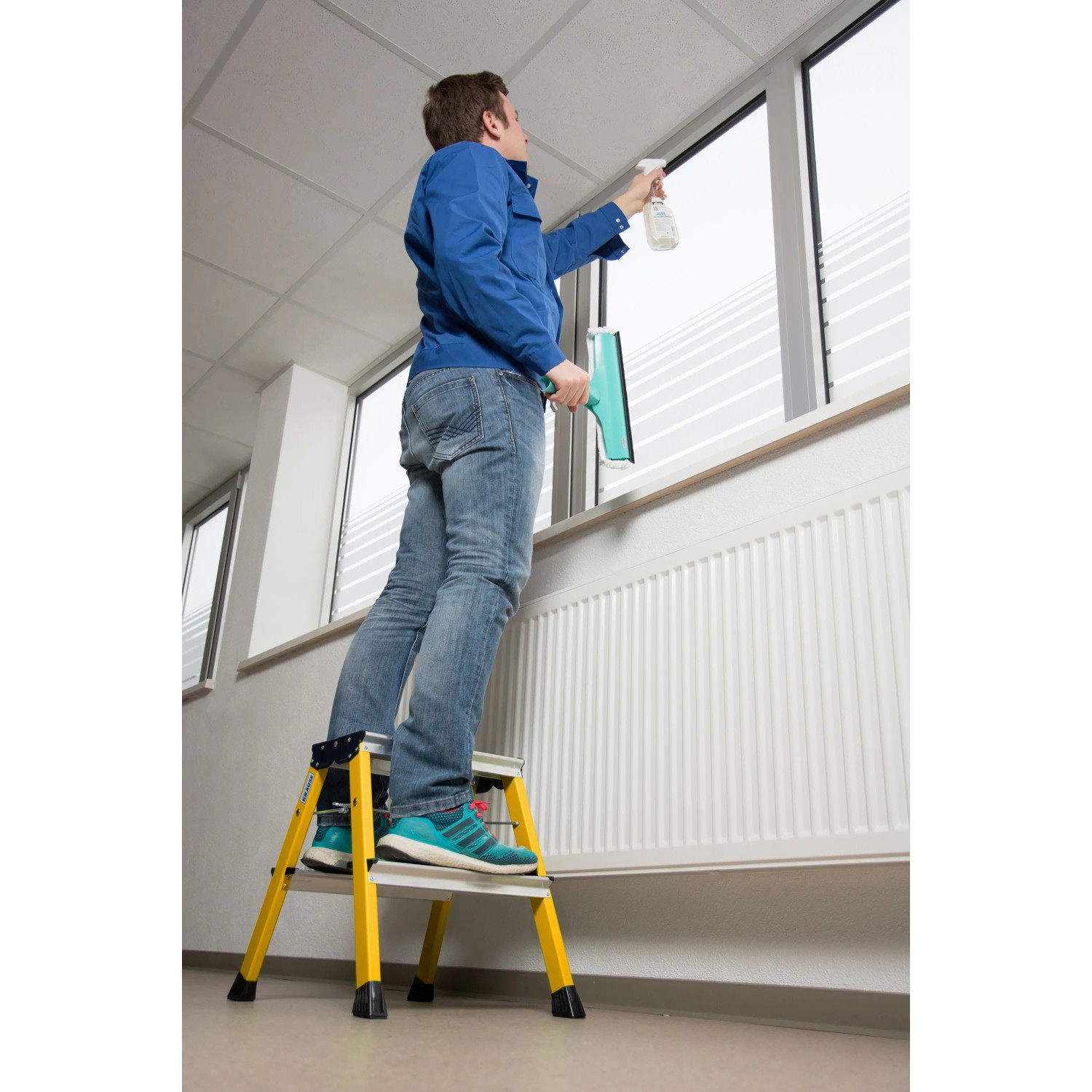 Mann reinigt Fenster stehend auf gelbem Krause Klapptritt Rolly 2x2 Stufen.