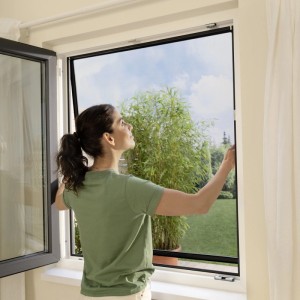 Frau montiert anthrazitfarbenes tesa Insect Stop Fliegengitter am Fenster.