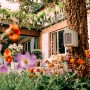 Elho Insektenhotel Cosy, beige-weiß, an Baum befestigt, umgeben von Blumen im Garten.