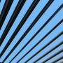 Detailaufnahme des Lamellendachs der anthrazitfarbenen Floraworld Pergola mit blauem Himmel im Hintergrund.