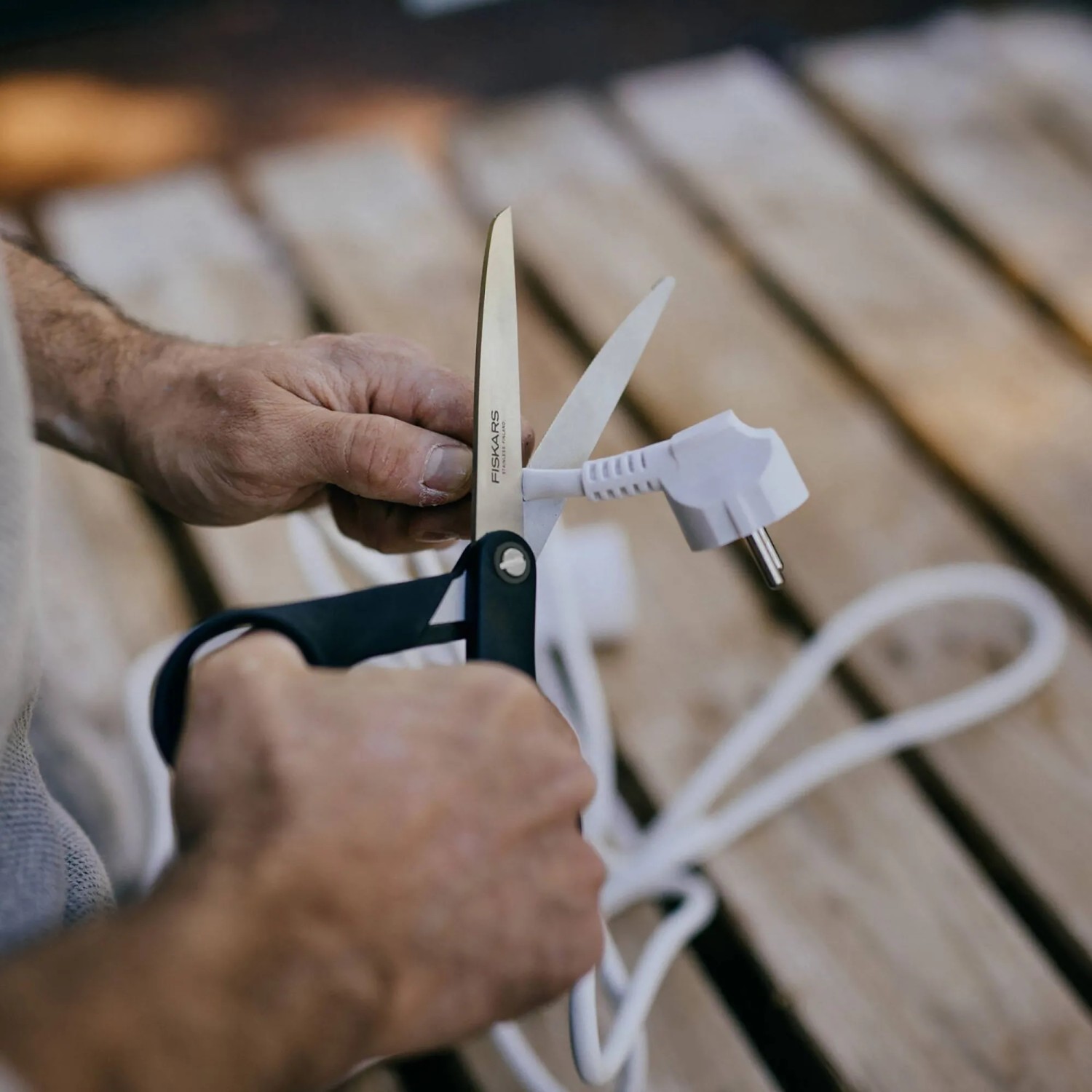 Mann schneidet mit Fiskars Hardware-Schere ein Stromkabel. 25 cm lange Schere mit schwarzem Griff.