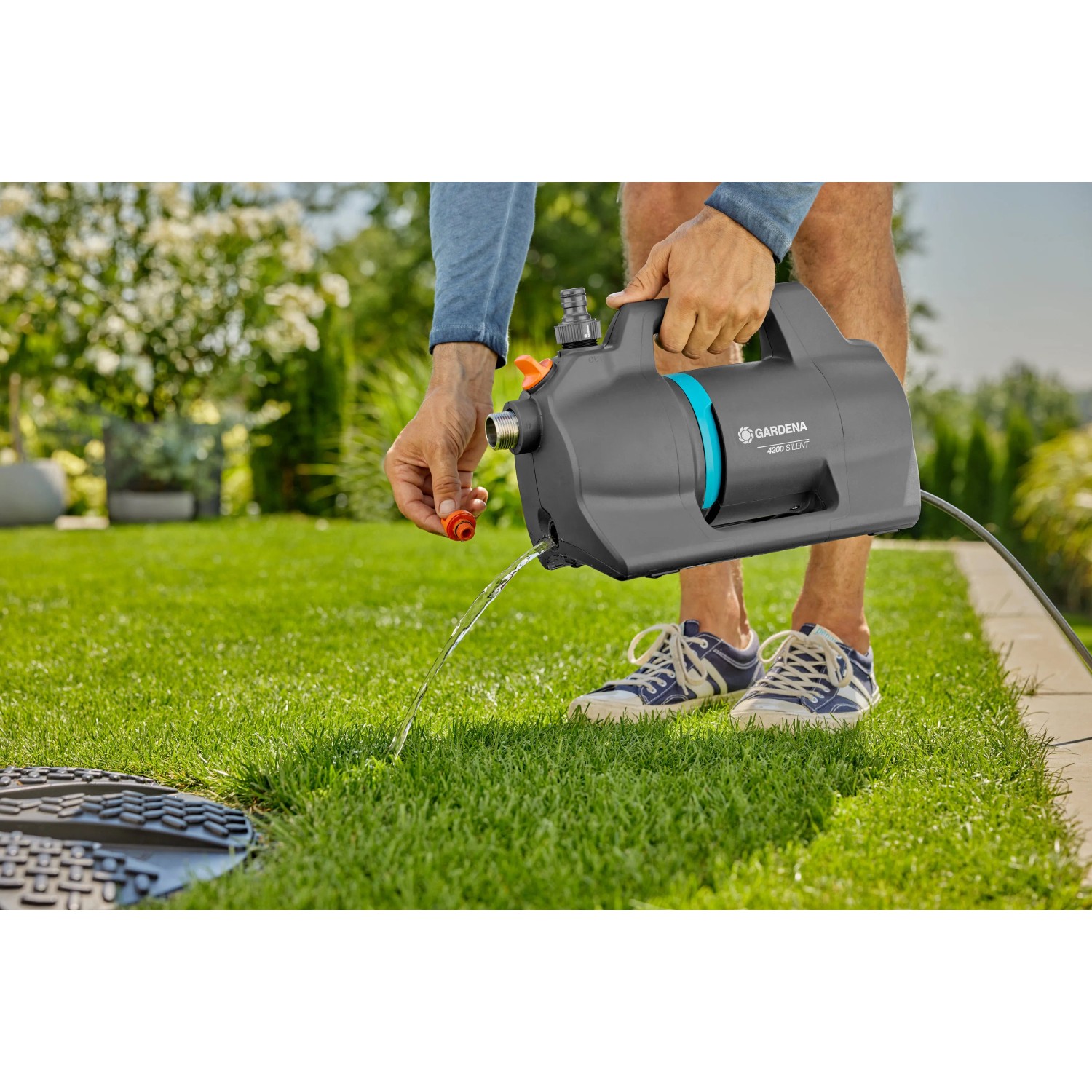Gardena Gartenpumpe 4200 Silent Set in Aktion: Graue Pumpe mit blauem Akzent pumpt Wasser in den Garten.