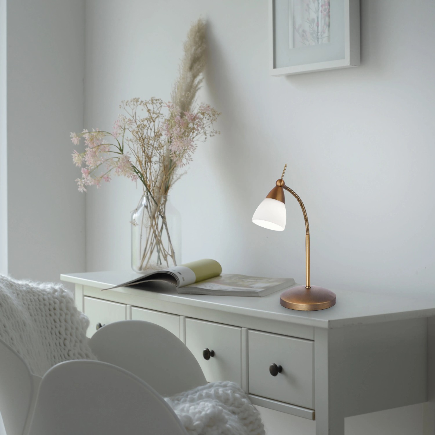 Paul Neuhaus LED-Tischleuchte Pino in Altmessing auf weißem Tisch. Schreibtischlampe mit Touchdimmer.