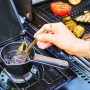 Char-Broil Gasgrill: Person bereitet Soße im Topf auf Seitenbrenner zu. Gegrilltes Gemüse im Hintergrund.