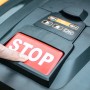 Hand drückt rote Stopptaste auf Yard Force EasyMow 260B Mähroboter.