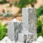Heissner Wasserspiel mit drei grauen Granit-Säulen und weißen Kieselsteinen im Garten.