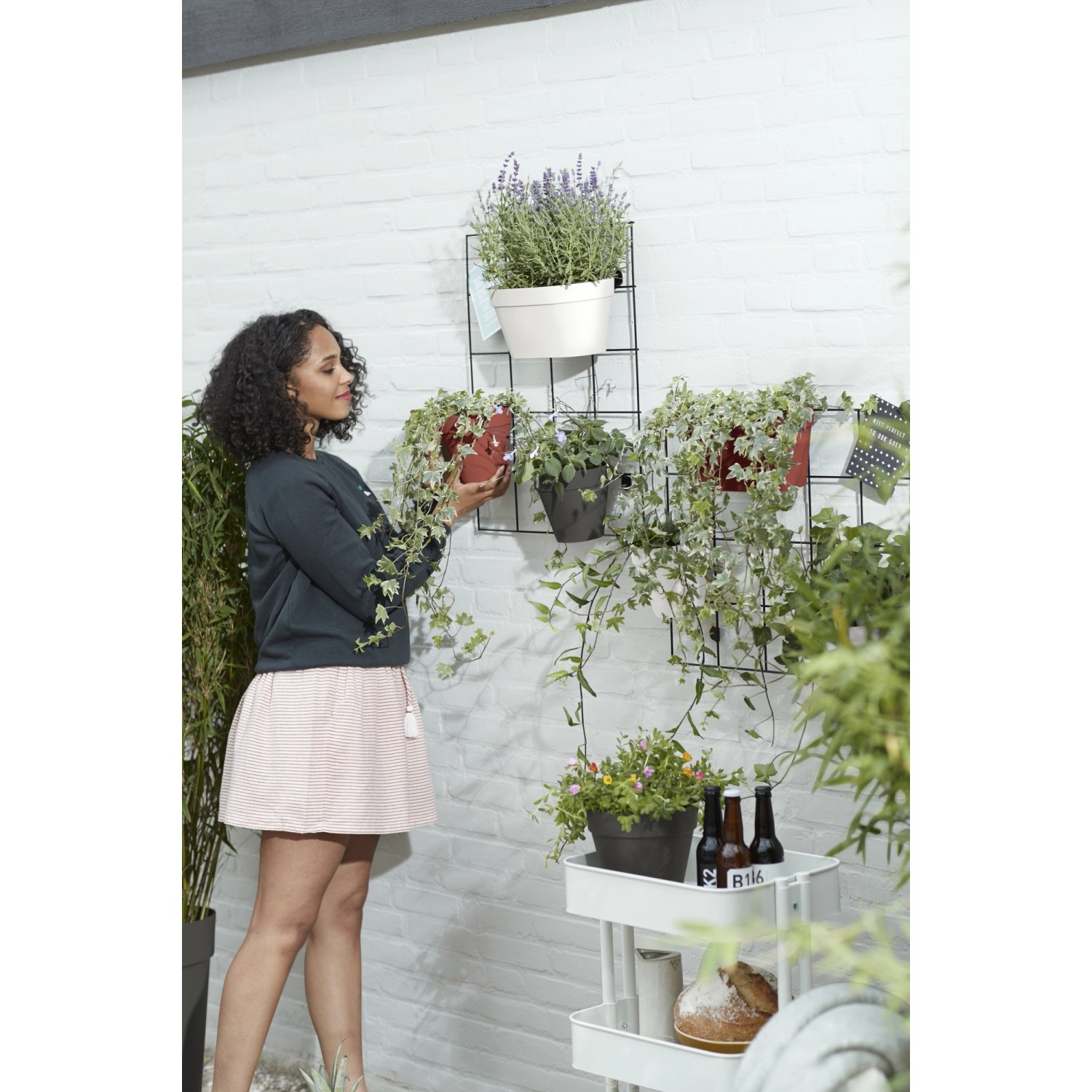 Frau bepflanzt Elho Wandhängetopf Loft Urban Duo (klinkerrot) am Wandgitter mit Pflanzen.