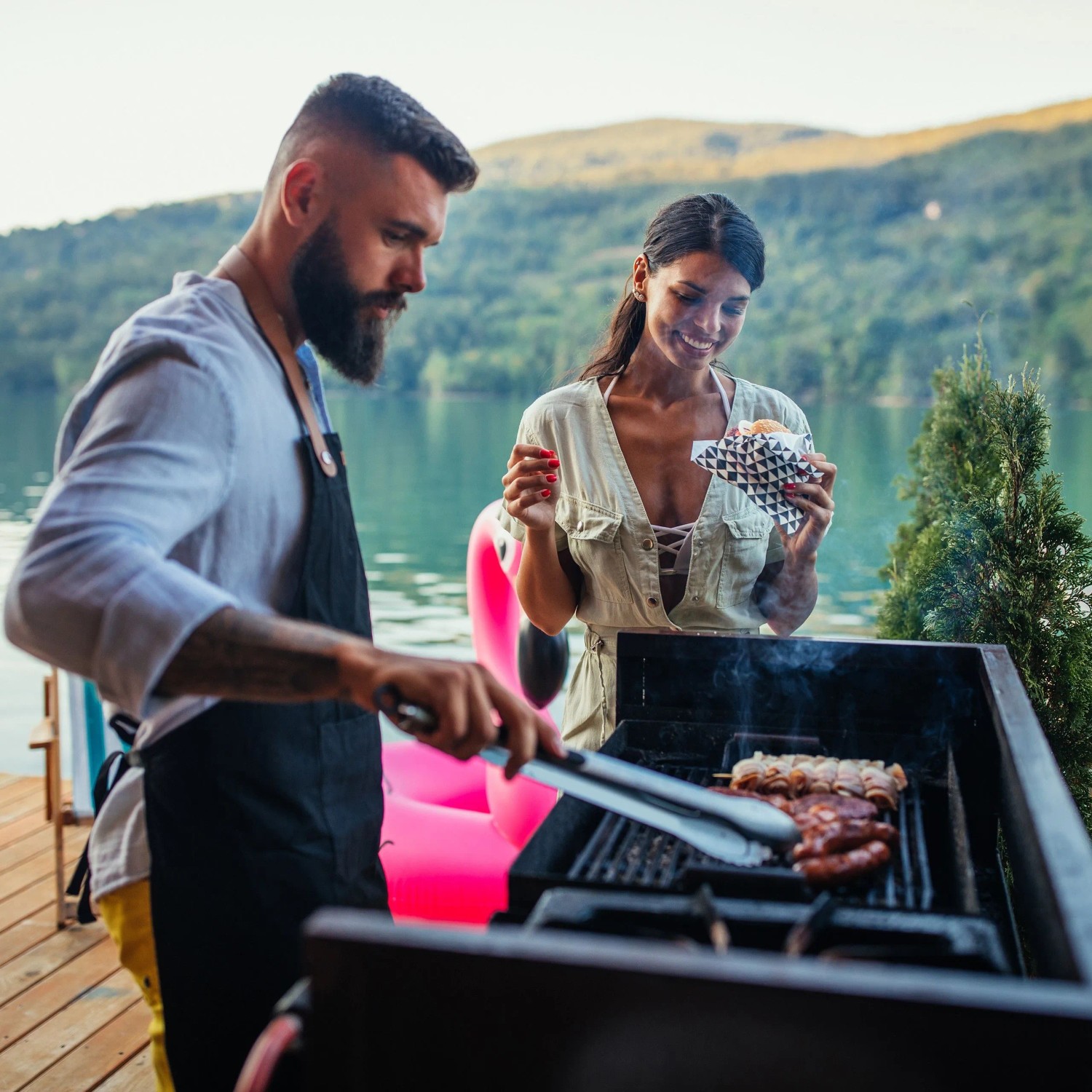 Mann grillt mit Grillzange Würstchen. Grillutensil aus Edelstahl mit Holzgriff.