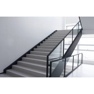 Treppenhaus mit grauen Stufen und schwarzem Geländer mit Glaseinsätzen.