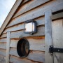 Moderne Lutec LED Solar-Wandleuchte Curtis mit Bewegungsmelder an einer Holzwand.