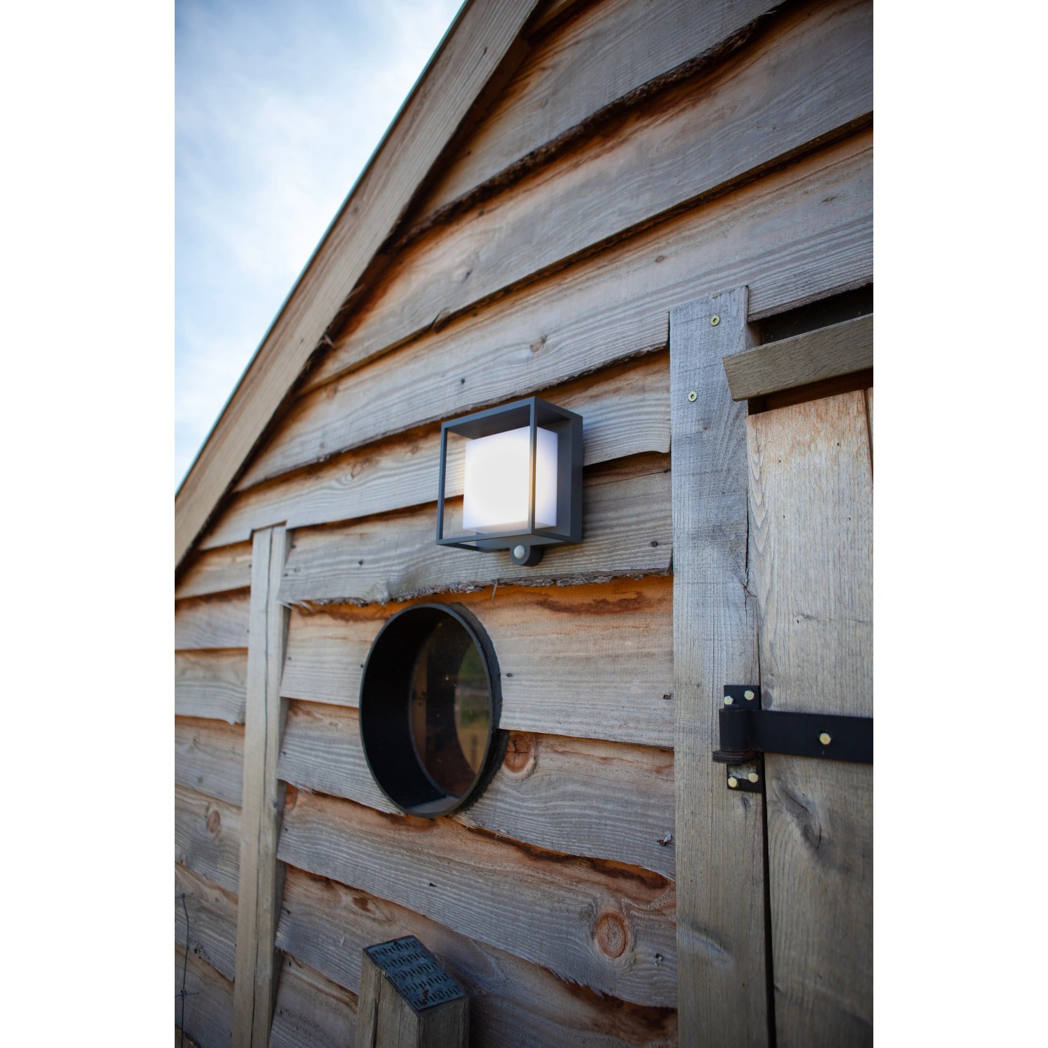 Moderne Lutec LED Solar-Wandleuchte Curtis mit Bewegungsmelder an einer Holzwand.