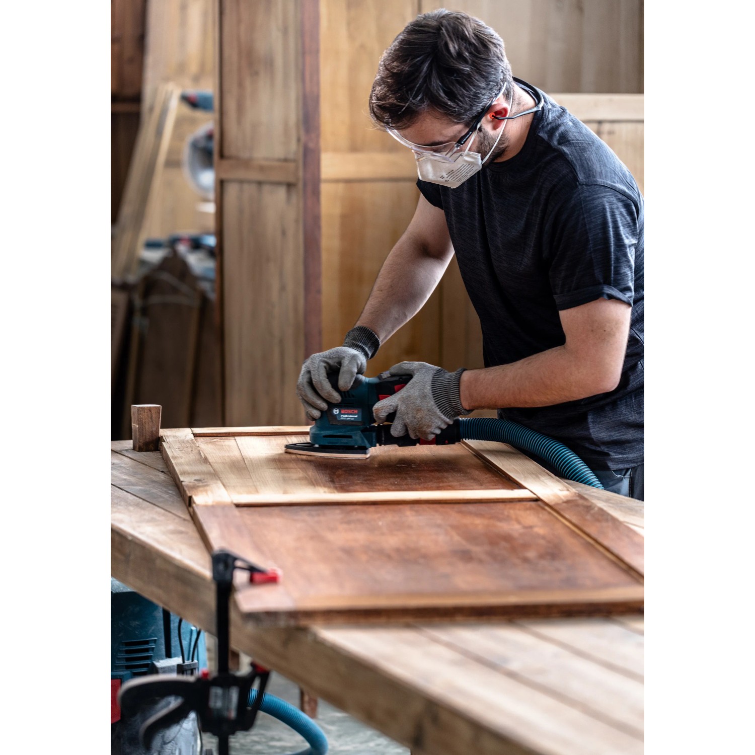Mann schleift Holz mit Bosch Exzenterschleifer und M480 Schleifblatt für staubarmes Schleifen.