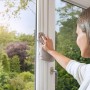 Frau reinigt Fensterrahmen vor der Montage eines Tesa Pollenschutzgitters.