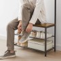 Songmics Garderobenständer Dacey mit Schuhbank, braun-schwarz. Person sitzt und bindet Schuhe.