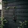 Fiskars Oszillierender Regner Comfort S-L, schwarz-orange, zur Gartenbewässerung an dunkler Holzwand.