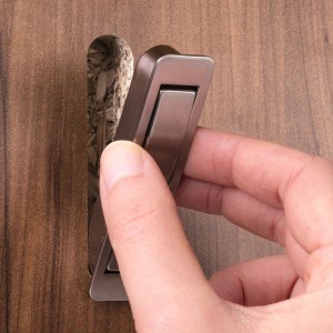 Hand klappt schwarzen SOTECH Klapphaken ZILLY aus Holzplatte. Versenkbarer Garderobenhaken zum Einfräsen.