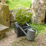 Quadratischer, anthrazitfarbener KHW Pflanzkasten mit Pflanze und Gießkanne im Garten.