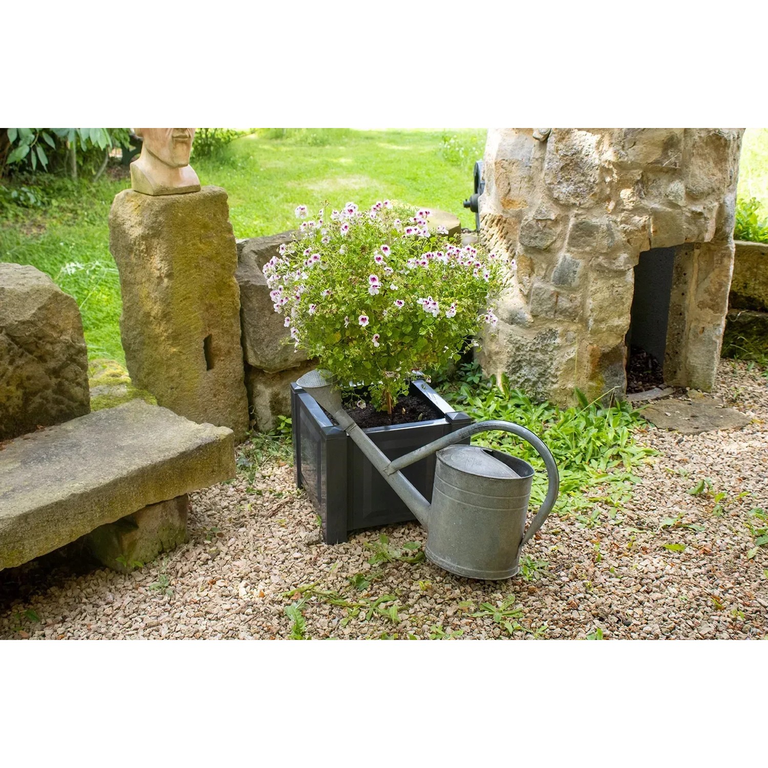 Quadratischer, anthrazitfarbener KHW Pflanzkasten mit Pflanze und Gießkanne im Garten.