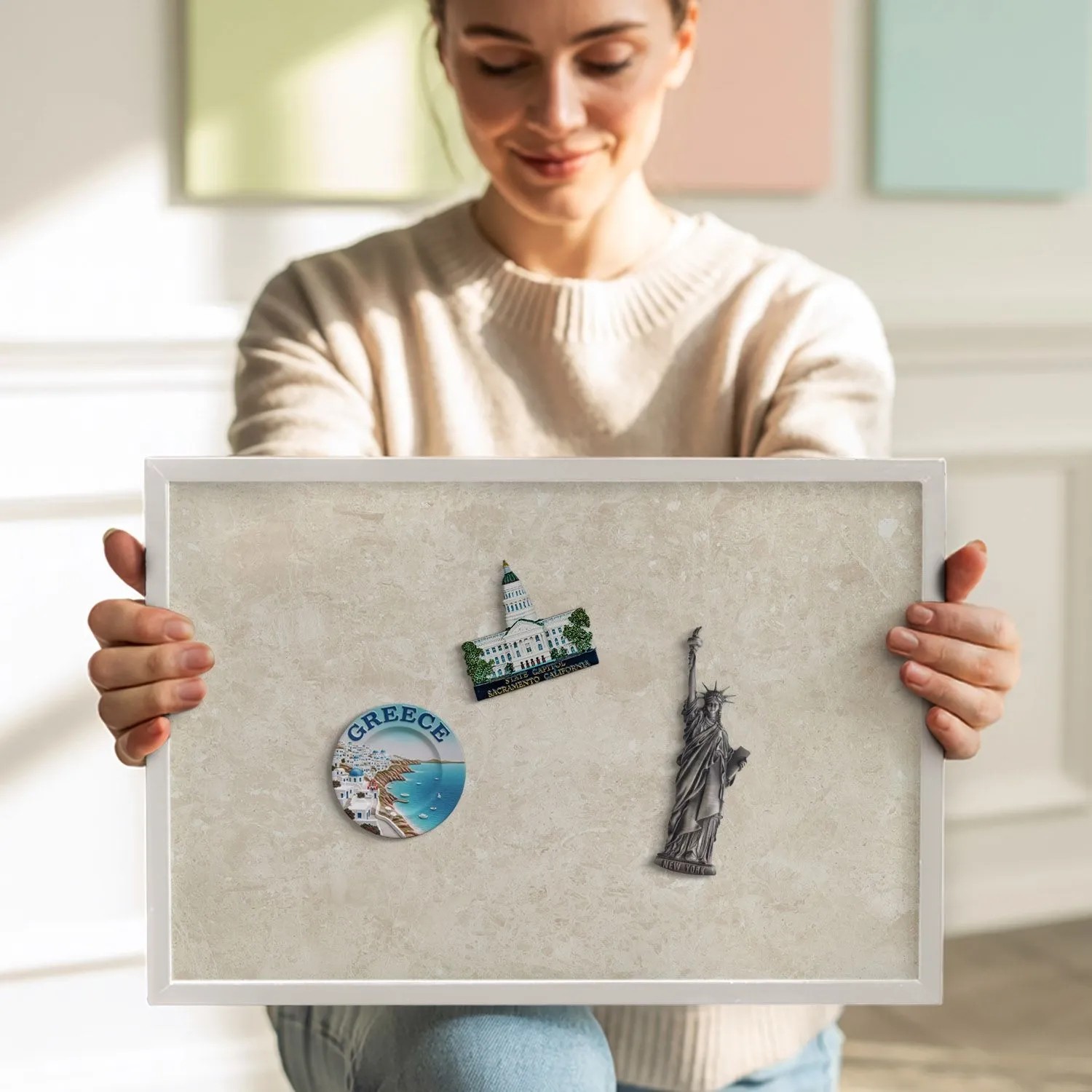 Lachende Frau hält weiße Tulup Magnettafel mit heller Steinoptik und Urlaubsmagneten. Gerahmtes Magnetboard für Notizen.