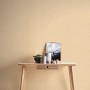Livingwalls Vliestapete Uni Creme-Beige an Wand über kleinem Tisch mit Deko.