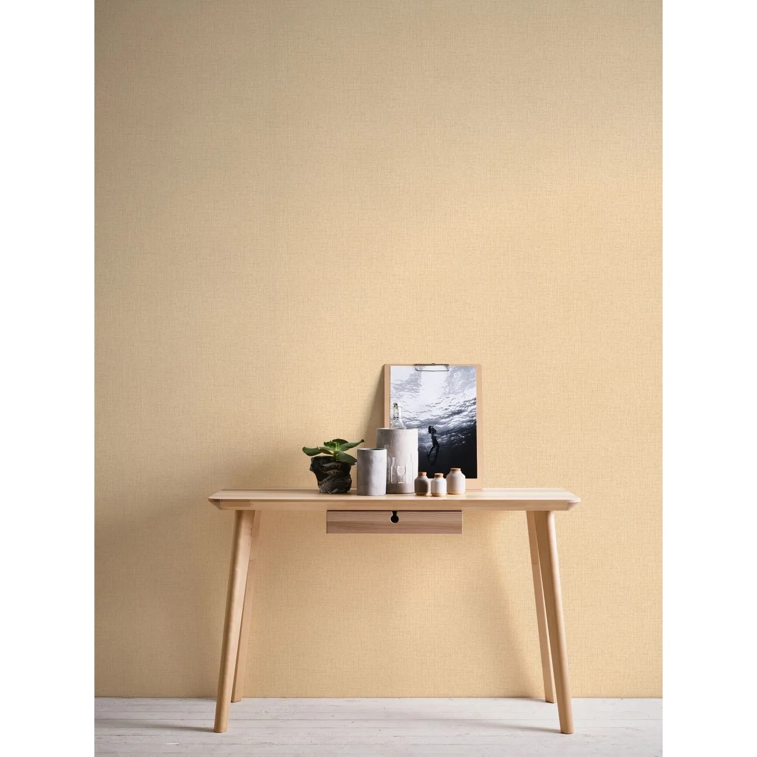 Livingwalls Vliestapete Uni Creme-Beige an Wand über kleinem Tisch mit Deko.