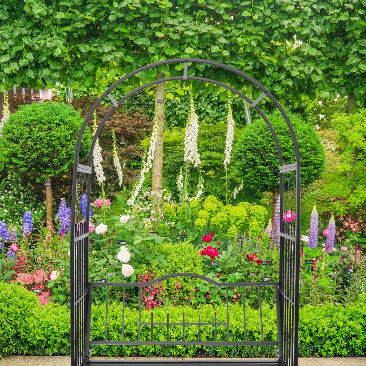 Schwarzer Eisen-Rosenbogen mit integrierter Sitzbank als Rankhilfe im grünen Garten. Perfekt für Kletterrosen.