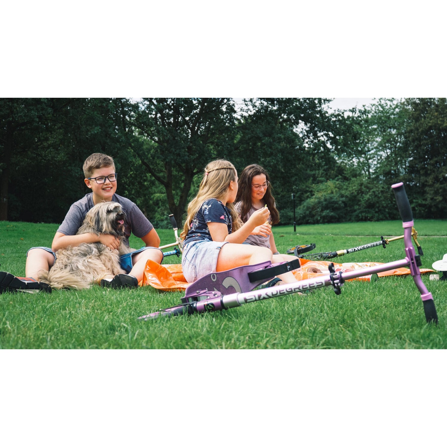 Hellblauer Six Degrees Scooter mit Kindern und Hund im Park. Klappbarer Aluminium Tretroller.