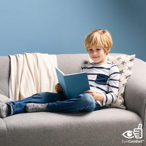 Junge liest Buch auf Sofa mit Decke und Kissen. Angenehmes Licht dank Philips LED.