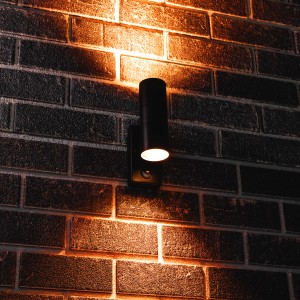 Schwarze, runde LED Außenwandleuchte mit IR-Sensor an einer Backsteinwand.