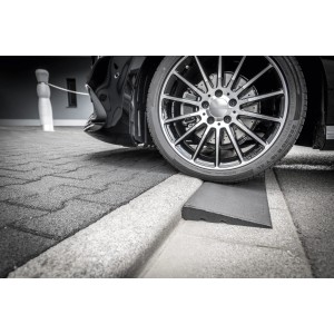 Schwarze Bordsteinrampe aus Gummigranulat unter einem Reifen, erleichtert das Auffahren.