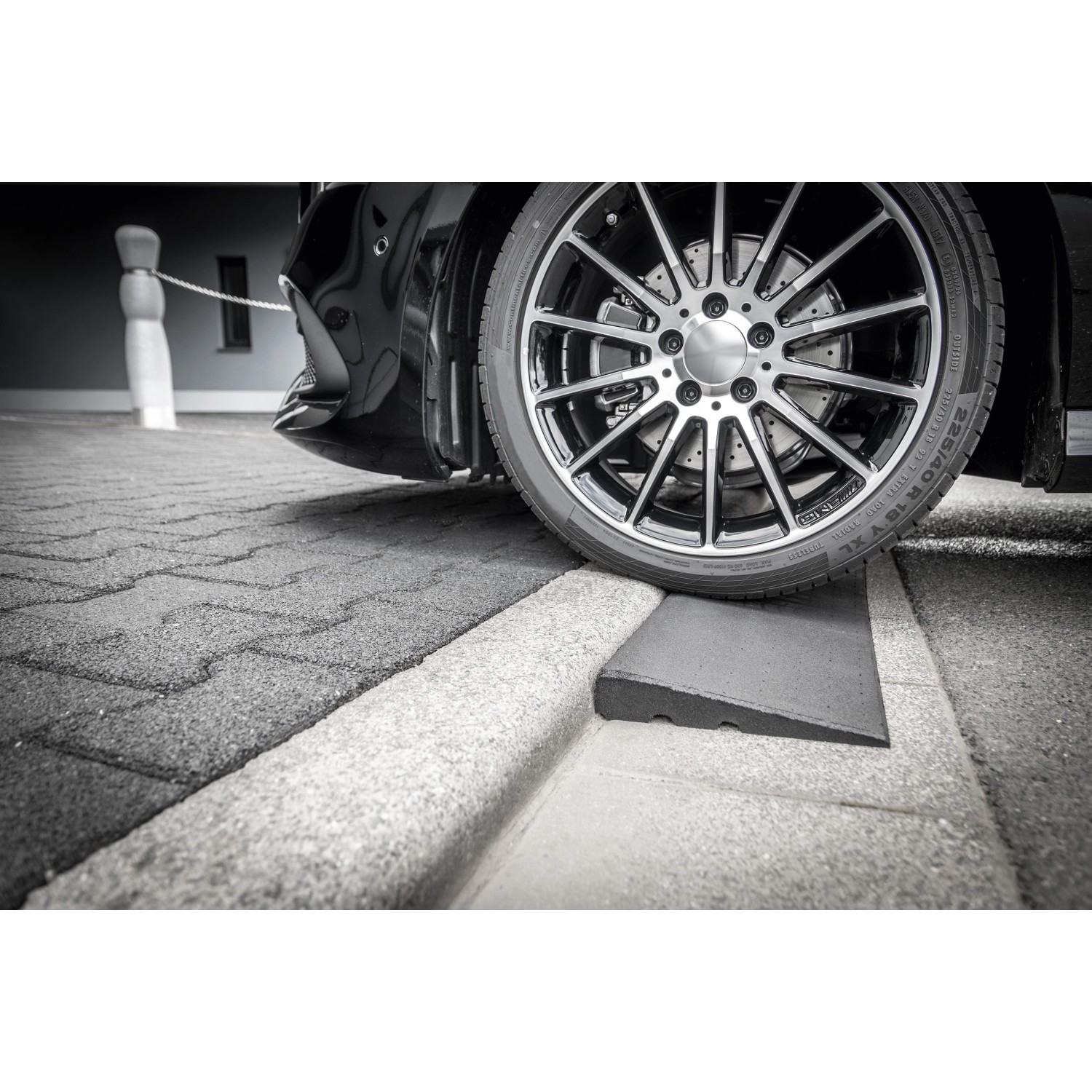 Schwarze Bordsteinrampe aus Gummigranulat unter einem Reifen, erleichtert das Auffahren.