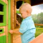 Kind öffnet Fenster vom Spielhaus Laura mit Leiter und Rutsche. Holzhaus mit grünen Akzenten.