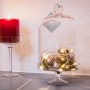 Dekorative LED Lichterkette von Konstsmide mit warmweißen Lichtern unter Glasglocke neben roter Kerze.