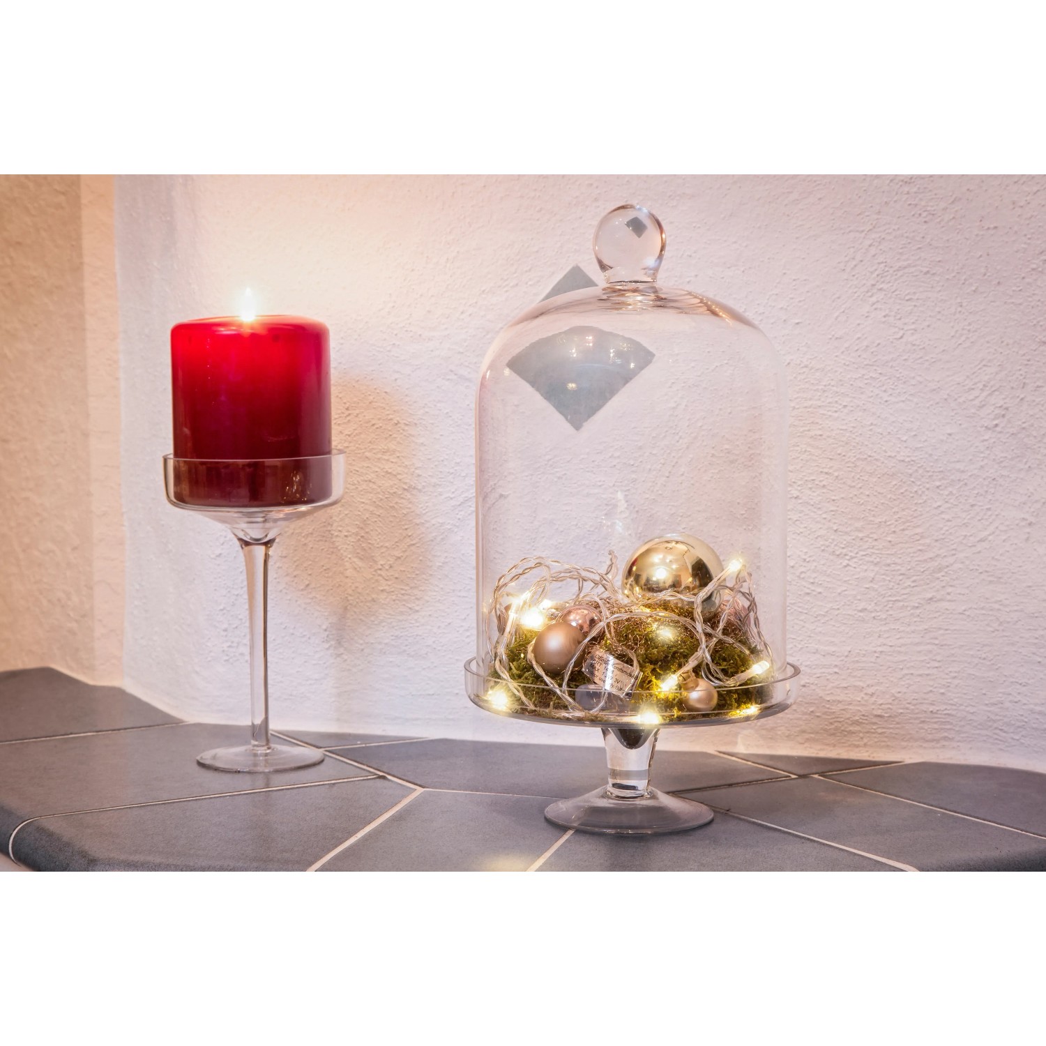 Dekorative LED Lichterkette von Konstsmide mit warmweißen Lichtern unter Glasglocke neben roter Kerze.