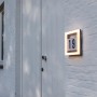 Quadratische LED Hausnummerleuchte Alice mit Hausnummer 19 an weißer Hauswand.