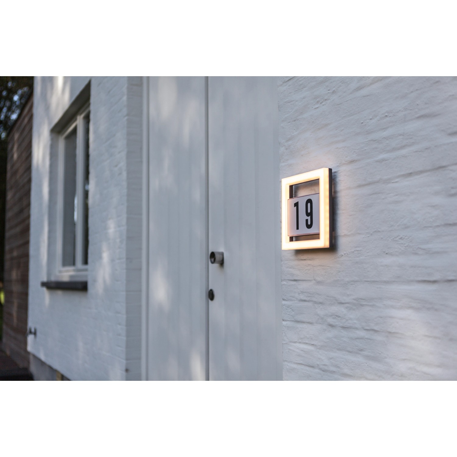 Quadratische LED Hausnummerleuchte Alice mit Hausnummer 19 an weißer Hauswand.