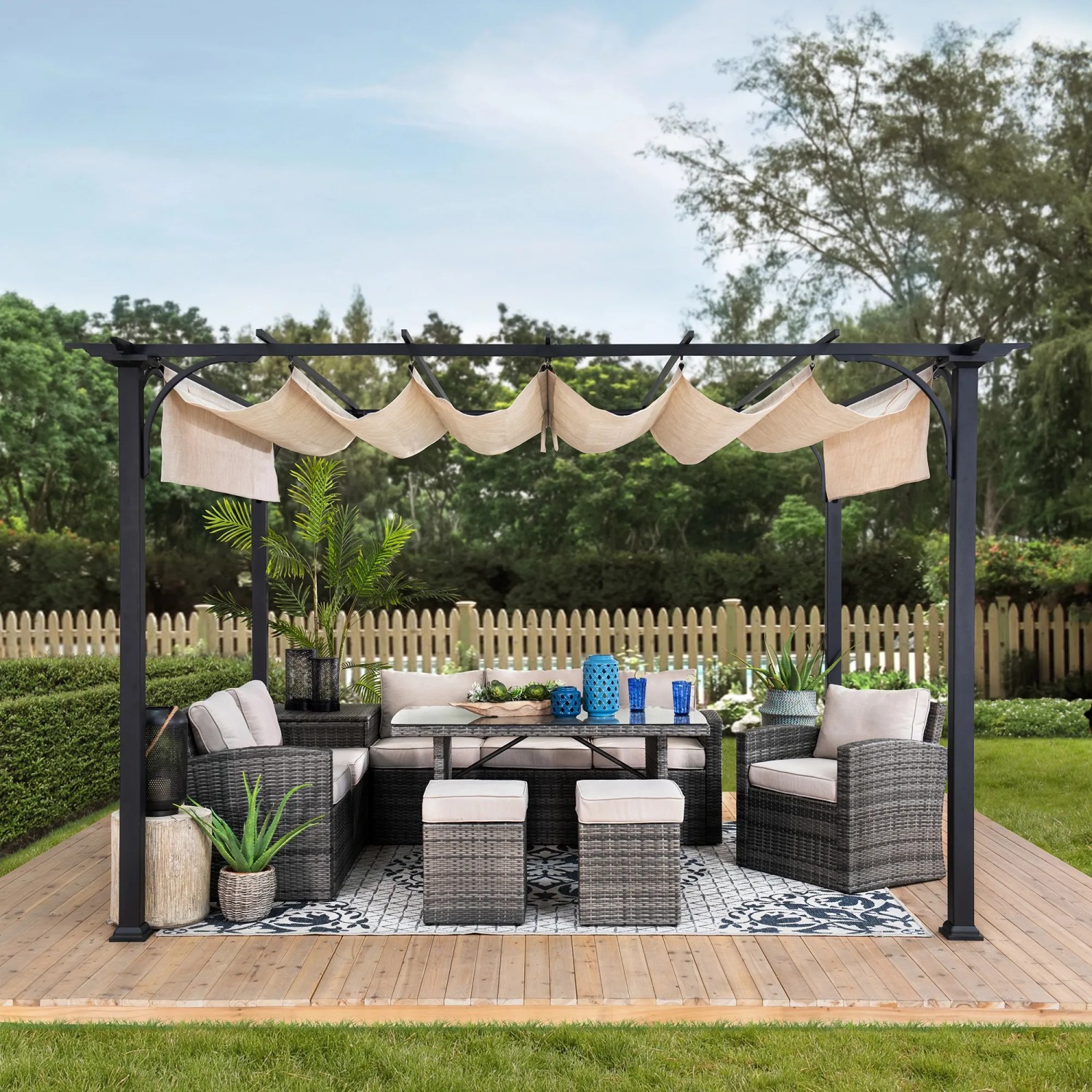 Weiße Sunjoy Pergola Giona aus Stahl mit beigem Stoffdach und Gartenmöbeln auf einer Holzterrasse.