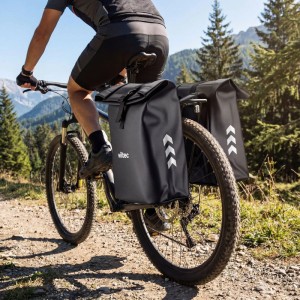 Schwarze Wiltec Doppeltasche am Fahrrad-Gepäckträger eines Mountainbikes auf Waldweg. Wasserfeste Fahrradtasche mit 48L Stauraum.