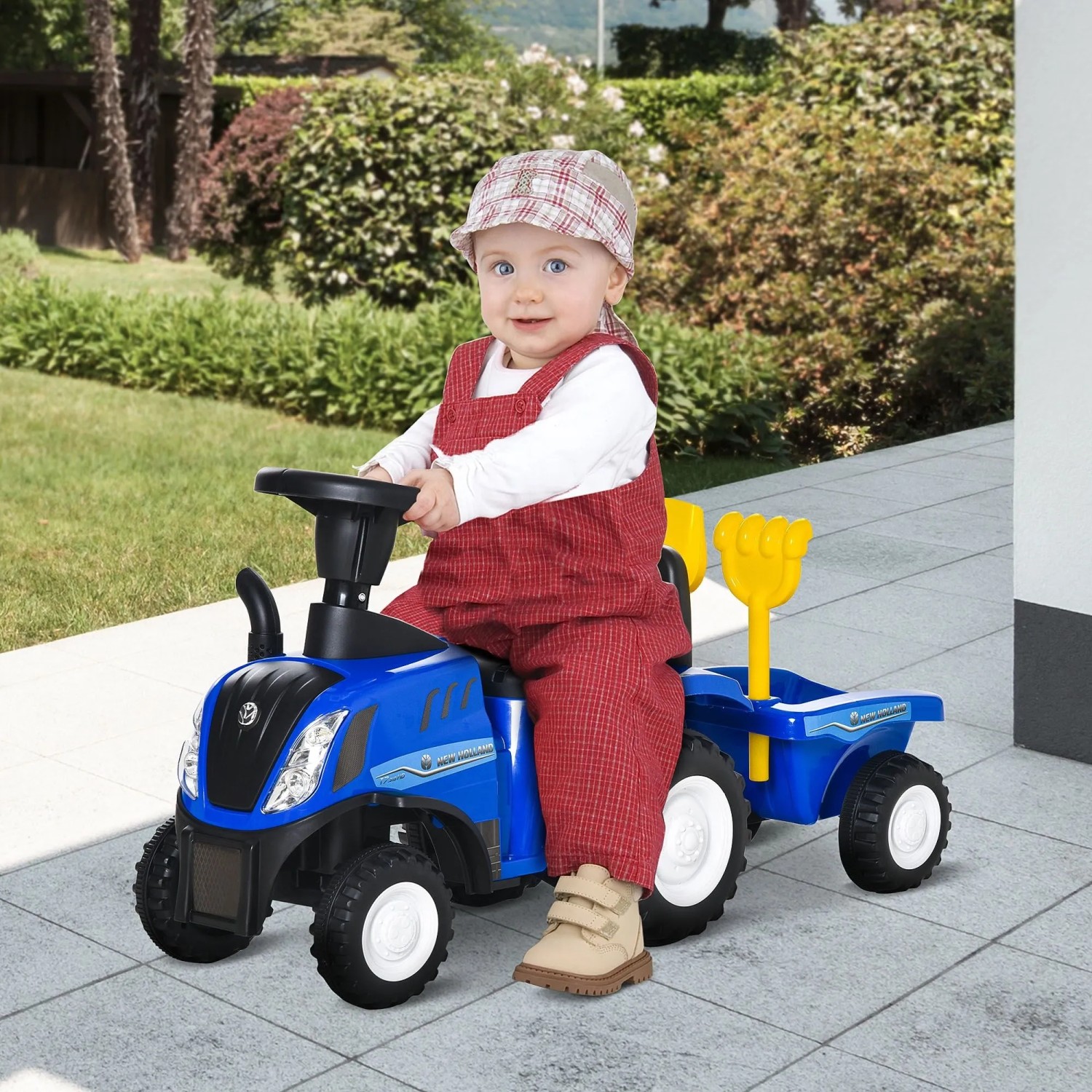 Kleinkind fährt blaues HOMCOM NEW HOLLAND Rutschauto Traktor mit Anhänger und Spielzeug im Garten. Ideal als Laufhilfe.